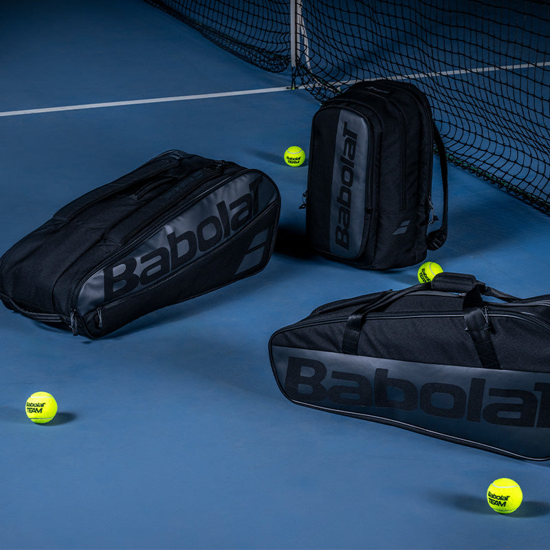 Babolat tennis bags on a blue court with a net and tennis balls