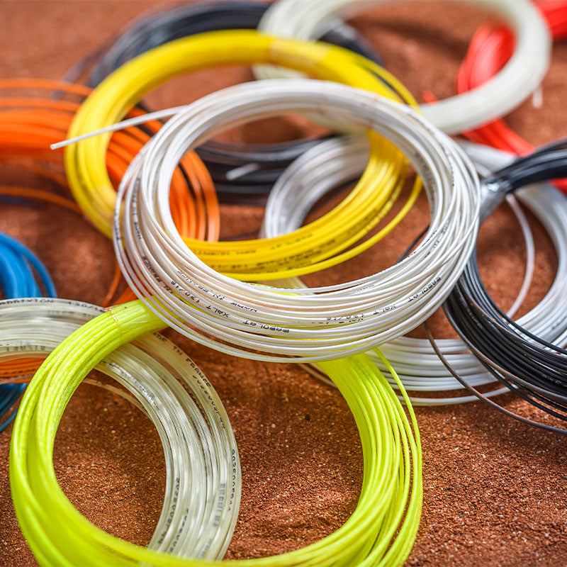 Loose Babolat tennis string sets of different colors on a clay court