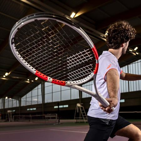 Lifestyle image: Mid-swing shot of a man playing with a Babolat Pure Strike 2024 tennis racquet on a dimly lit indoor court.