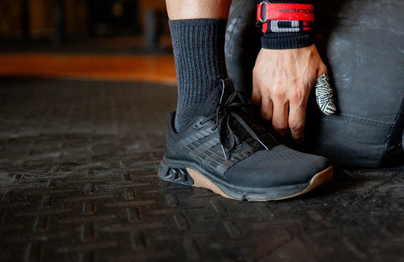 Lifestyle image of a person lifting weights in a gym wearing black inov8 F-Lite training shoes